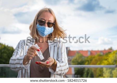 A young woman in an anti-covid mask stands on a terrace of her house, holding a disinfectant gel in her hands. Woman in terrace with sanitizer gel. Woman in quarantine on terrace. Pandemic theme