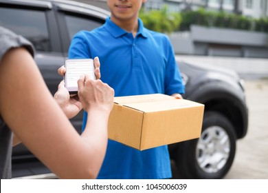 Young woman appending signature in digital mobile phone after receiving parcel from courier at home.