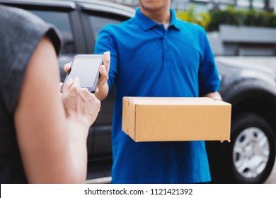 Young Woman Appending Signature In Digital Mobile Phone After Receiving Parcel From Courier At Home.