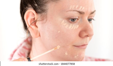 Young woman applies concealer makeup on her face with a small brush. Similar to foundation, or color corrector, is a type of cosmetic used to mask dark circles, age spots, large pores, and other small