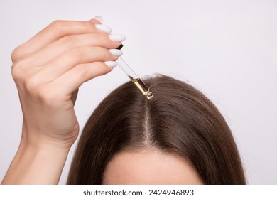 A young woman applies a drop of oil from a pipette to her scalp, close-up. Vitamins, keratin for treatment, strengthening and growth of hair. Problems with dandruff, hair loss. Hair care concept
