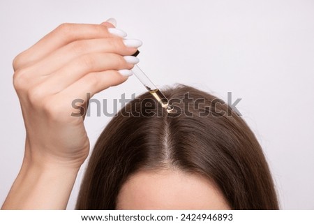A young woman applies a drop of oil from a pipette to her scalp, close-up. Vitamins, keratin for treatment, strengthening and growth of hair. Problems with dandruff, hair loss. Hair care concept