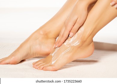 a young woman applies lotion to her feet on white towel - Powered by Shutterstock