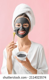 Young Woman Applying Activated Charcoal Mask On Her Face Against Color Background