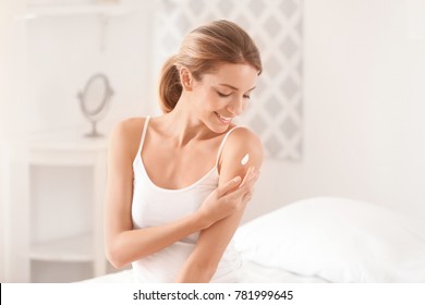 Young woman applying body cream at home