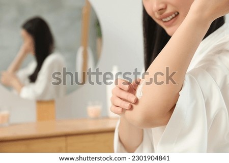 Young woman applying body cream on elbow in bathroom, closeup. Space for text