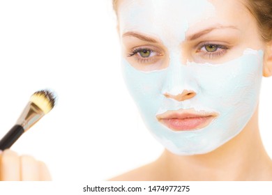 Young woman applying with brush green mud mask to face, on white. Teen girl taking care of oily skin, purifying the pores. Beauty treatment. Skincare.
