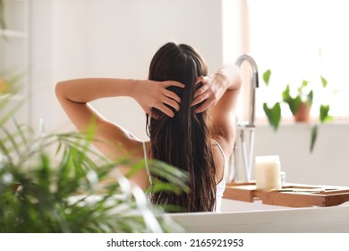 Mujer joven aplicando aceite de coco en su cabello en el baño