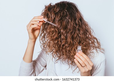 Young Woman Applying Cosmetic Oil To Her Beautiful Curly Hair, Close-up On White Background.