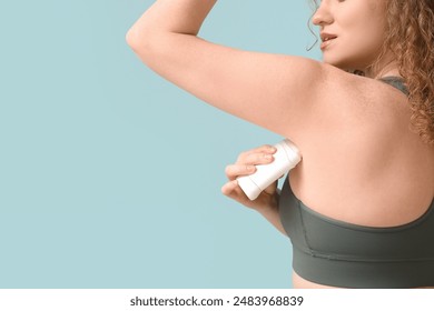 Young woman applying deodorant on blue background, closeup