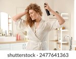 Young woman applying dry shampoo on her hair in bathroom