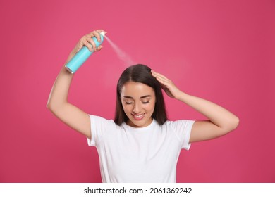 Young woman applying dry shampoo against pink background - Shutterstock ID 2061369242