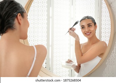 Young woman applying dye on hairs near mirror indoors - Shutterstock ID 1875268504