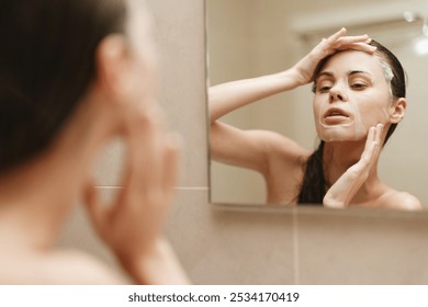 Young woman applying face mask in front of mirror, focusing on skincare routine and self-care at home. Daily beauty practice and wellness theme. - Powered by Shutterstock