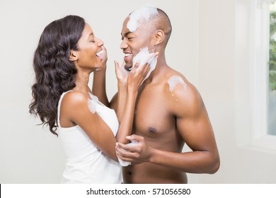 Young woman applying foam on young mans face in the bathroom - Powered by Shutterstock