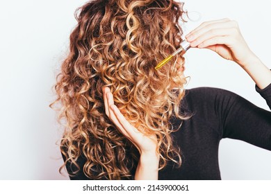 Young Woman Applying Hair Care Oil To Her Curly Hair Tips