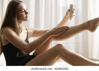 young woman applying lotion to legs - Powered by Shutterstock