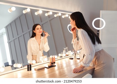 Young woman applying make up near illuminated mirror indoors - Shutterstock ID 2120479253