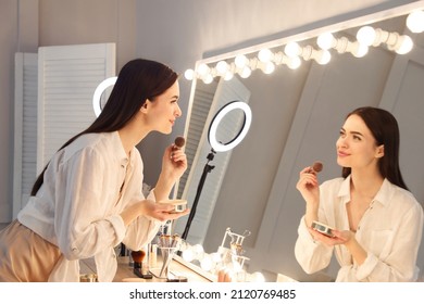 Young woman applying make up near illuminated mirror indoors - Powered by Shutterstock