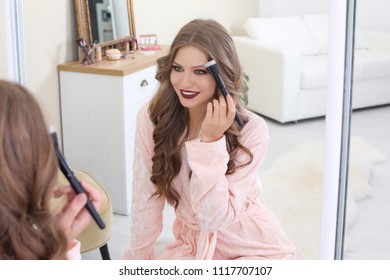 Young woman applying makeup near mirror in dressing room