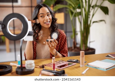 Young woman applying makeup on face with brush while recording vlog on smartphone for social media with LED ring lamp on table. Multiethnic fashion makeup artist vlogger live streaming makeup tutorial - Powered by Shutterstock