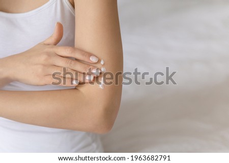 Young woman applying moisturizing body lotion on smooth skin of arm. Hand of girl massaging shoulder and elbow with natural nourishing soft cream. Skincare, dermatology concept. Close up, copy space