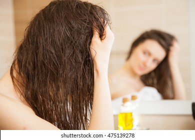 Young Woman Applying Oil Mask To Hair Tips In Front Of A Mirror; Haircare Concept