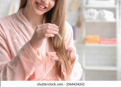 Young Woman Applying Oil Onto Hair In Bathroom