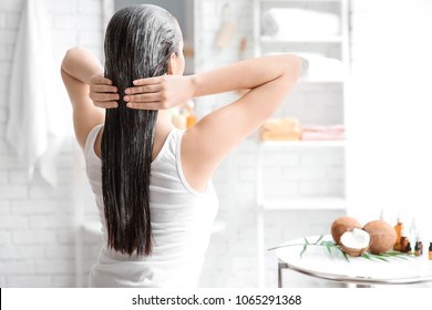 Young woman applying oil onto hair in bathroom