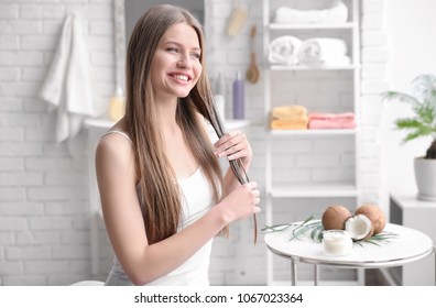 Young Woman Applying Oil Onto Hair In Bathroom