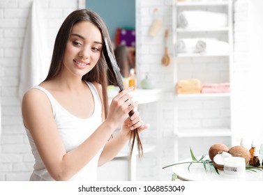 Young Woman Applying Oil Onto Hair In Bathroom