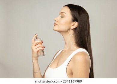 Mujer joven que aplica perfume sobre fondo blanco
