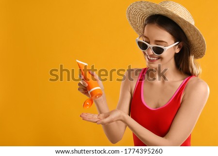 Young woman applying sun protection cream on orange background