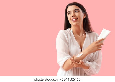 Young woman applying sunscreen cream on pink background - Powered by Shutterstock