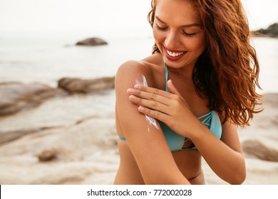 Young Woman Applying Sunscreen Lotion On The Beach