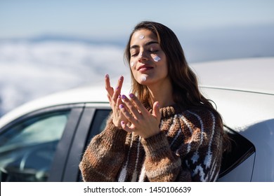 Young woman applying sunscreen on her face in snowy mountains in winter, in Sierra Nevada, Granada, Spain. Female wearing winter clothes.