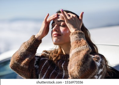 Young Woman Applying Sunscreen On Her Face In Snowy Mountains In Winter, In Sierra Nevada, Granada, Spain. Female Wearing Winter Clothes.