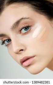 Young woman applying three color samples of facial foundation cream at her face. Beauty model with perfect fresh skin and long eyelashes cares about her skin at home. Skin Care Concept.