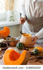 Young Woman In Apron Preparing Delicious Homemade Pumpkin Soup On Her Kitchen. Fresh Organic Ingredients, Traditional Autumn Food. Healthy Eating, Cozy Home Atmosphere