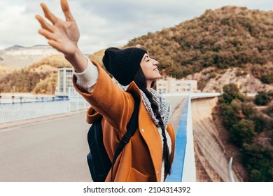 Young Woman Arms Outstretched By The Mountain At Sunrise Enjoying Freedom And Life, People Travel Wellbeing Concept. Cheerful Smiling Woman Wearing Winter Clothes Enjoying At The Top Of Dam.
