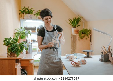 Young woman artisan potter holding a vase standing in workshop. Selective focus. - Powered by Shutterstock