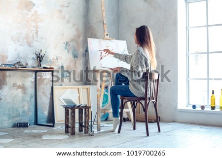Young woman artist painting at home creative painting back view
