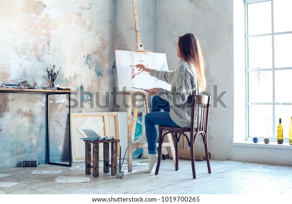 Young woman artist painting at home creative\
painting back view