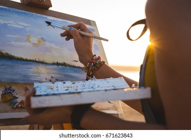 Young woman artist painting landscape in the open air on the beach, close up