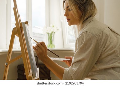 Young Woman Artist Painting On Canvas On The Easel At Home Studio