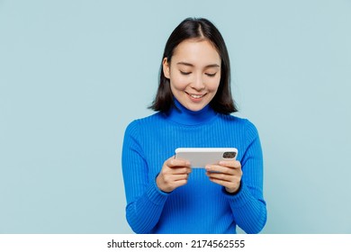 Young Woman Of Asian Ethnicity 20s Wears Blue Shirt Using Play Racing App On Mobile Cell Phone Hold Gadget Smartphone For Pc Video Games Isolated On Plain Pastel Light Blue Background Studio Portrait