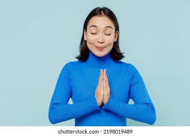 Young Woman Of Asian Ethnicity 20s Years Old Wears Blue Shirt Hands Folded In Prayer Gesture Begging About Something Keeps Eyes Closed Isolated On Plain Pastel Light Blue Background Studio Portrait