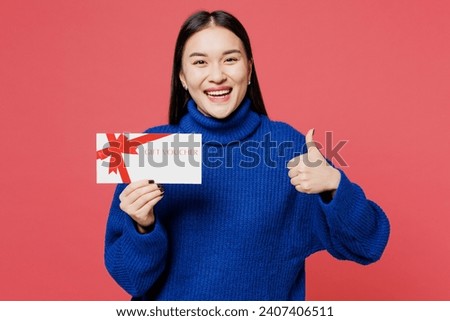 Young woman of Asian ethnicity she wear blue sweater casual clothes hold gift certificate coupon voucher card for store show thumb up isolated on plain pastel light pink background. Lifestyle concept