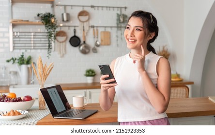 Young woman Asian happy and interested in thinking using mobile phone in kitchen room.