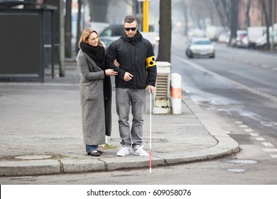 Young Woman Assisting Blind Man With White Stick On Street